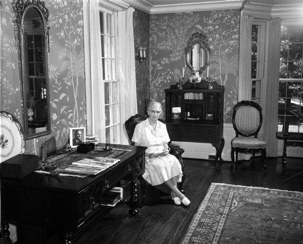 Leslie Gillett is sitting in her traditional antique-filled living room at 3443 Edgehill Parkway in Shorewood Hills. The home will be featured in the Attic Angels Association Home Tour on July 14, 1955.