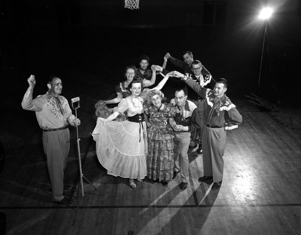 The "Allis Promanaders," a square dancing group that meets in the gym of Frank Allis school, hold a public square dancing party for the benefit of the Empty Stocking Club. Fritz Erb is the caller, and Mr. and Mrs. Ralph George duck through the arch. Other couples from front to back include: Mr. and Mrs. Robert Beckman, Mrs. Fritz Erb and Paul Payne, and Mr. and Mrs. Garwood Mather. Admission to the party was one new doll or a stuffed toy.