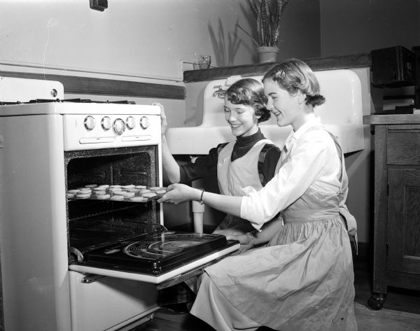 Susie Kamm and Nancy Miles putting cookies into the oven. The girls are members of the 8th grade home economics class at West Junior High School. The class baked several thousand Christmas cookies for the patients at the Veteran's Administration Hospital.