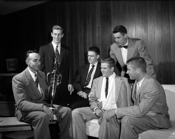 Wisconsin High School football players and their coach admiring the Gene Wheeler Memorial Trophy they received at a football banquet at the East Side Business Men's Clubhouse. Left to right: Coach Hal Metzen, John Coombs, Bob Patterson and Bill Thomas. Toastmaster Jack Sprague and Chuck Thompson are standing. John Coombs and Chuck Thompson shared honors as most valuable players.
