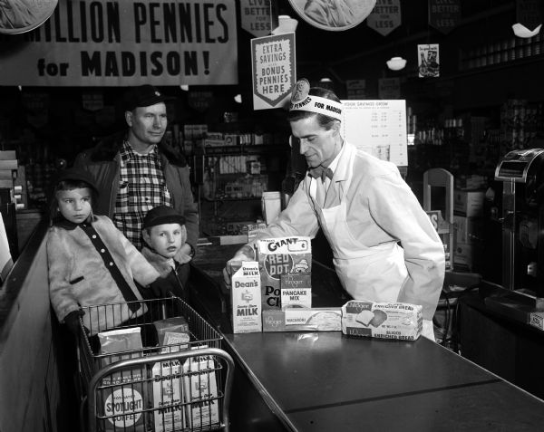A father and two children at the Kroger grocery store check out counter purchase Dean's milk, Red Dot potato chips, Kroger pancake mix, macaroni, and bread.