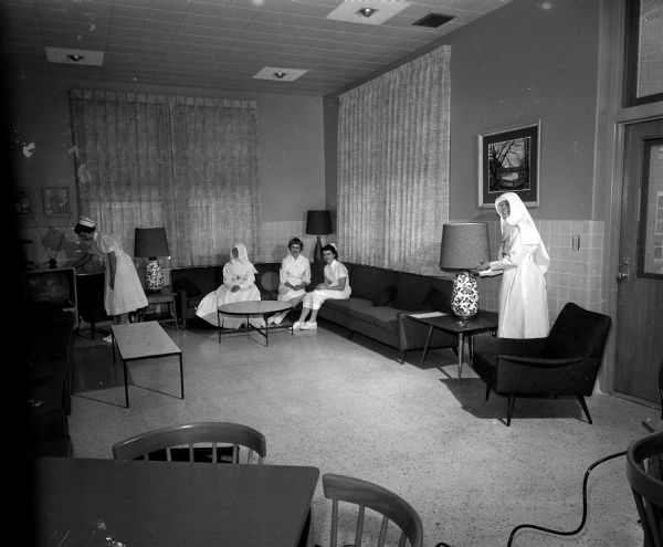 The original caption states: "here, trying out the comfortable setting of the patients' living room are Irene Gruendler, Sister Mary of the Angels, Mary Ellen Rose, Virginia Schmitt, and Sister Kenneth Marie. All five women are registered nurses."