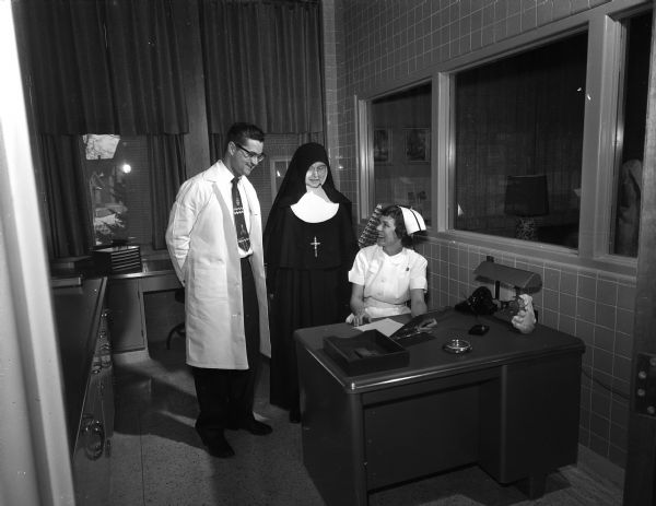 Dr. Edward Bruckner, pathologist, Sister Mary Seraphia, S.S.M., administrator of the hospital, and Eleanor DeMeuse, supervisor nurse, conferring in the glassed-in nursing station of the new center.