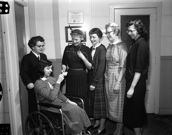 Members of the Four Lakes Secretaries Association present a check for $100 to Mary Mills, a victim of polio, seated in a wheelchair. The money will help defray her expenses as a student of Madison Business College. Left ro right:  Barbara Thompson, chair of the project committee; Marion Dengel, president: Paula Feschenich, committee member; Annette Rasmussen, vice-president; and Mrs. Paul Woerpel, committee member.