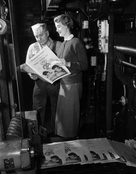 Nancy Staudenraus, "Wisconsin State Journal" librarian and assistant Spelling Bee director, and Ernest P. Green, day foreman of the press room, looking at the "Wisconsin State Journal" brochure, "It is Time to Start the 1954 Badger Spelling Bee."