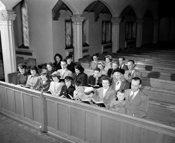Stanley and Nora Mockrud and their eight children sit in a front pew at Bethel Lutheran Church, 312 Wisconsin Avenue. The children (left to right) are: Nola, 18; Annnette, 15; Nancy, 13; Karen, 12; Solveig, 10; Roald, 9; Mary, 6; Karl, 3. They lived at 209 North 7th Street and were participating in the beginning of Family Week in Madison.