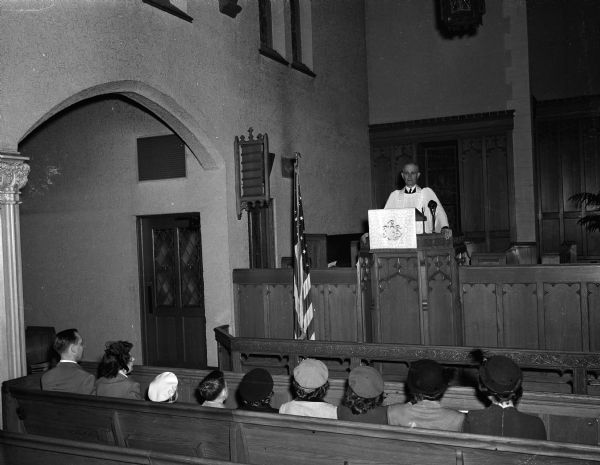 Mr. and Mrs. Mockrud and their eight children sitting in a front pew at Bethel Lutheran Church while the pastor is standing in the pulpit. The youngest child is on Mr. Mockrud's lap and not visible in this view. The Mockrud's lived at 200 North 7th Street.