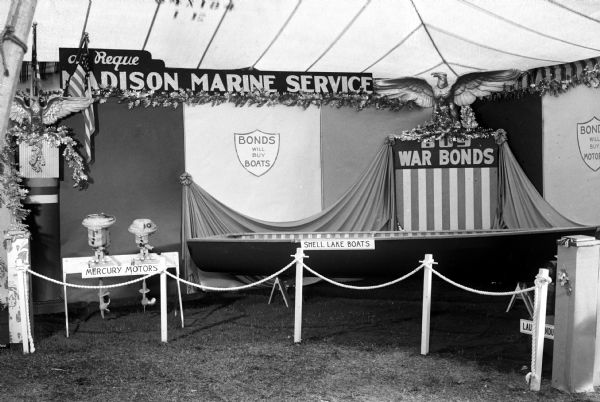 View of Albert Reque's Madison Marine Service Booth at the Eastside Festival with banner "Buy War Bonds" and "Bonds Will Buy Boats." The booth also features Shell Lake boats and Mercury motors.