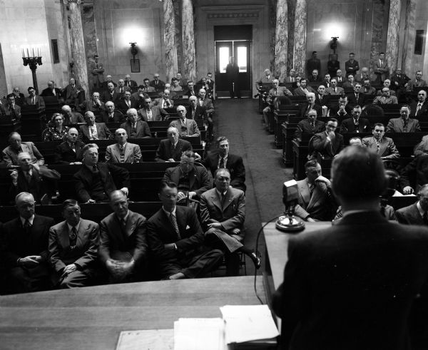 The Wisconsin State Legislature listens to a speech by Governor Walter J. Kohler, Jr. The senators are seated in the first row, with Warren Knowles seated in the aisle.