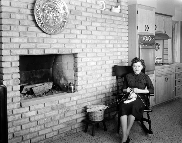 Mrs. Harvey (Bonita) Hubanks sitting next to a fireplace in the family room adjacent to the kitchen in their home at 4206 Jerome Street in Madison. The kitchen can be seen over her shoulder in the background. This is one of ten kitchens that were part of a kitchen tour to raise funds for foreign exchange students at Monona Grove High School.