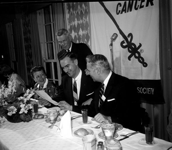 Pictured at the speakers' table at the dinner at Maple Bluff Country club are, left to right: Juliana Luberg; Dr. W.D. Stovall, director of the State Laboratory of Hygiene; Dr. Robert Samp, a staff member at University Hospital, and LeRoy Luberg, President of the board of the Dane County Unit of the American Cancer Society, master of ceremonies. Behind them is a microphone and a banner with the society's logo.