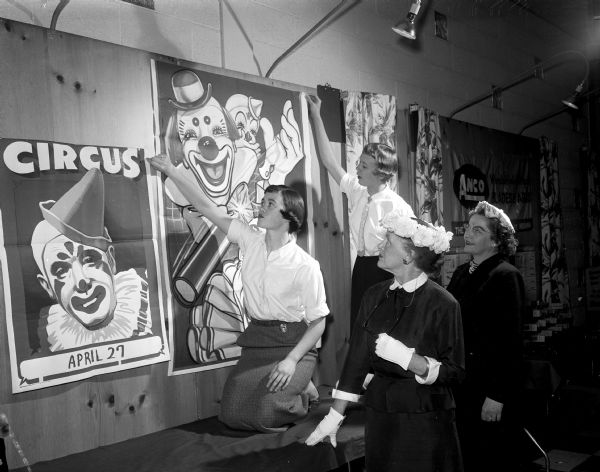 Mary Ellen Lathers, Judy Angevine, Alnora M. Lathers, and Jessie C. De Woody apply circus posters to the interior walls of the East Side Business men's clubhouse in preparation for the annual Beaux Arts Ball, sponsored by the Madison Art Association.