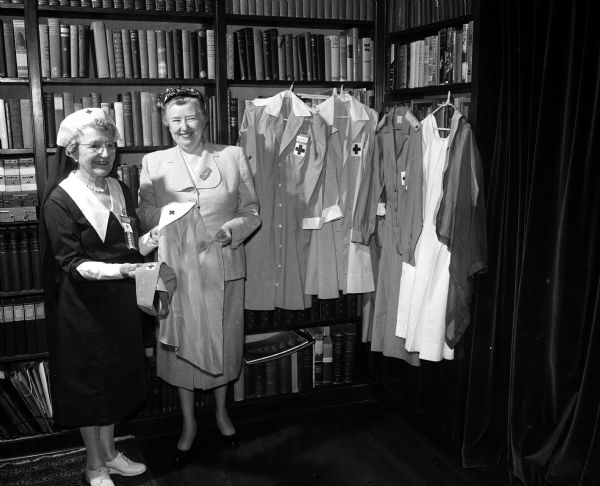 Selma L. Schubring and Dorothy C. Schar model Red Cross uniforms spanning forty years of service. Uniforms include a Braillist one, staff aide volunteer uniforms, a Red Cross production worker's uniform, and the Gray Lady gown.