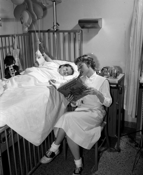 Junior Aide volunteer Kathleen Hensen reading a story to 4-year-old Jennifer Bahowick at her bedside in Madison General Hospital.