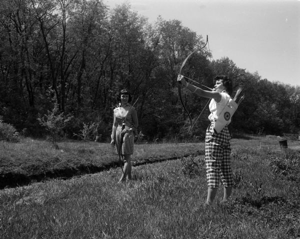 Dorothy L. Day and Ruth E. Van Tassel show off their form as archers. They and their husbands are members of the Blackhawk Archery Club.