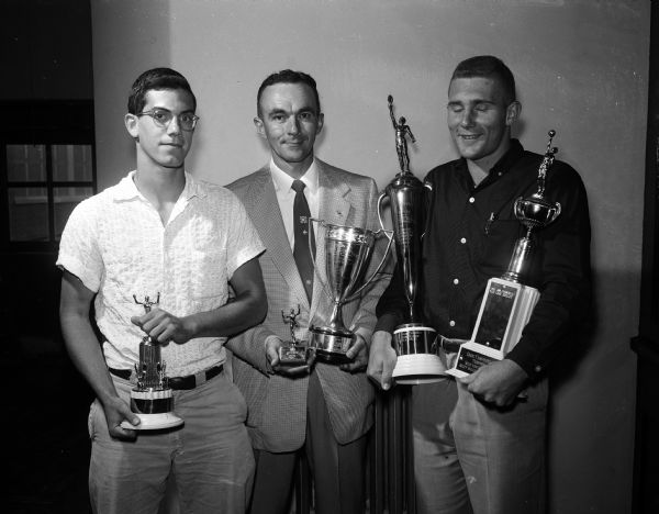 Group portrait of Wisconsin High School sports coach Hal Metzen with trophy winners Phillip (Pete) Cohen (left), and Dick Pauley (right). Five trophies are shown, four having been won by Pauley.