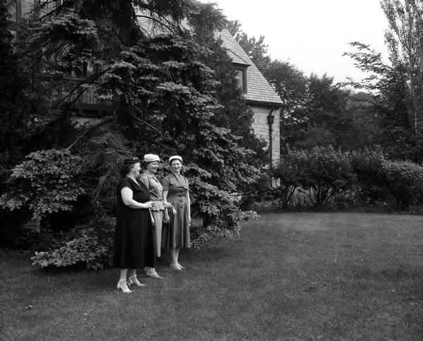 Three women who will preside at serving tables for the open house of Bishop William P. O'Connor's residence are looking over the pleasant gardens behind the house on Lake Mendota at Fox Point. Left to right are Catherine Burke, Mrs. Edward Linden, and Alice Osborne.
