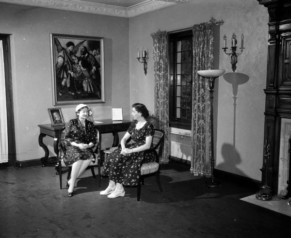 Myrtle Bond and Eileen Kohls visit in a corner of the living room of Bishop William P. O'Connor's residence on Lake Mendota at Fox Point. They will be helping at the open house for more than 1,000 women of the seven-county Madison diocese. Behind the women is a painting of St. Raphael, the patron of the Catholic parish.