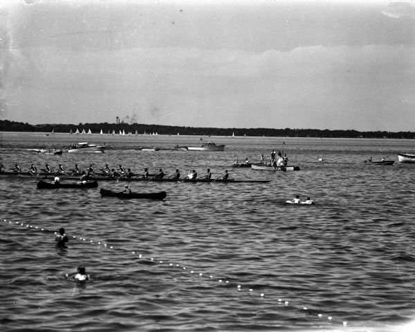 Action shot of the University of Wisconsin vs. Stanford varsity crew race on Lake Mendota. Stanford's crew, in the foreground, pulls across the finish line half a length ahead of Wisconsin.