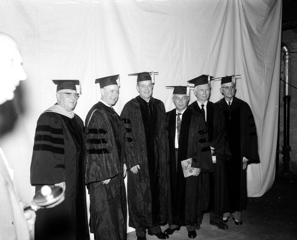 Six men wearing caps and gowns attend the University of Wisconsin graduation ceremonies.