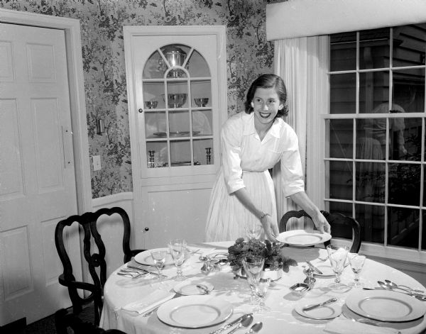 Mary Weston Frautschi preparing her dining room table for a dinner party. The photograph is one of a series showing how newlywed women have made their new living space attractive and hospitable.