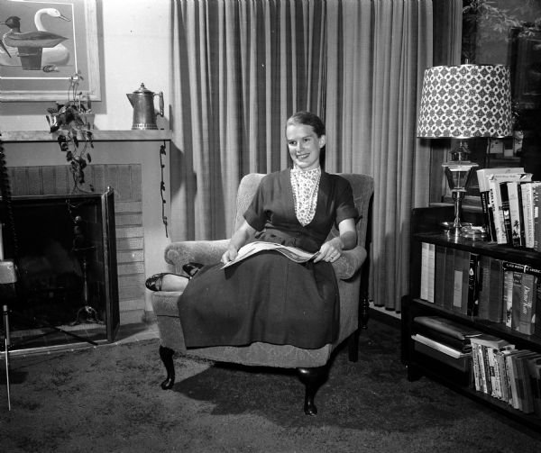 Portrait of Mary Jean Du Bois Holland, sitting in a corner of her living room. The photograph is one of a series showing how newlywed women have made their new living space attractive and inviting for themselves and their husbands.