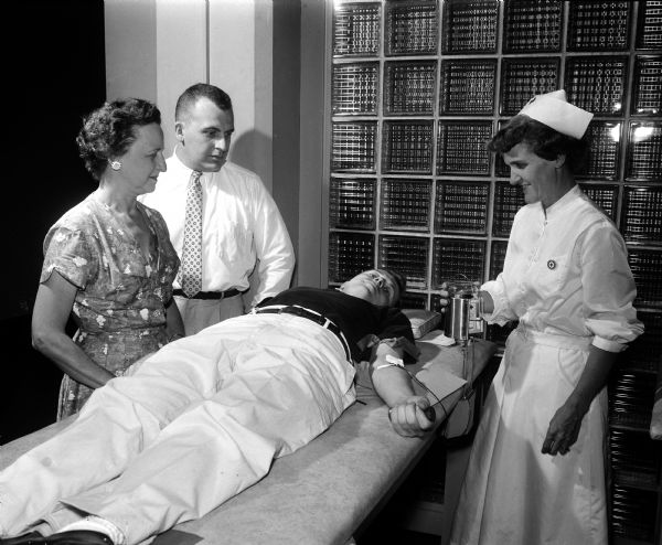 George Gill gives a pint of blood for the Red Cross as his mother, Florence, and brother, James, look on. The Red Cross nurse is Valdine Prentice.