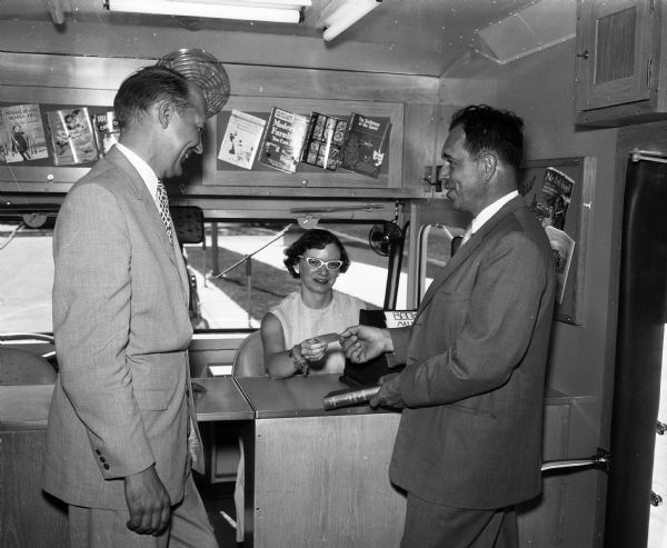 Interior of Madison Public Library's new bookmobile. Librarian Doris Cruger is sitting at the desk inside Madison Public Library's new bookmobile. Standing are Mayor Ivan Nestingen (left) and Board Member Thomas J. Stavrum (right).