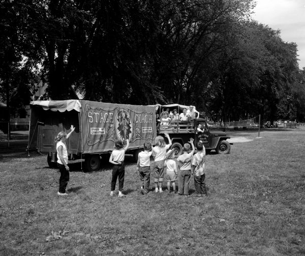 The Stage Coach, presented to the teen-aged theatrical group in 1951, is parked at the Marquette School playground. Performers and students in attendance are waving farewell at the end of the Madison Youth Summer Theater season.