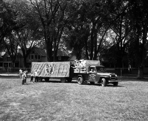 The Stage Coach and truck used for the Madison Youth Summer Theater driving past a playground. Students who watched the performance are waving to the actors as they leave after the final play of the season.