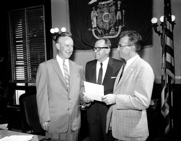 Governor Vernon Thomson (left) is handing a letter of appointment to Francis J. Walsh to be the acting director of the State Bureau of Personnel. In the center is the current director, Volmar Sorensen, who is resigning.