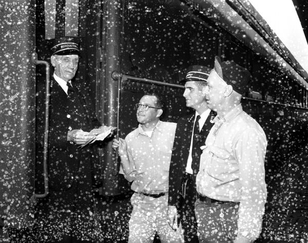 While standing on the steps of a passenger car, North Western Railway conductor C.R. Odekirk is preparing for his final run on the Dakota 400. He is retiring after 52 years with the railway. Looking on, left to right, are A.C. Meyer, fireman; F.C. Seils, brakeman; and C.H. Nelson, engineer.