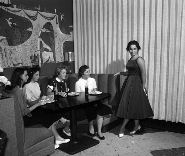 Four teenage girls admire a formal dress presented at the Vogue fashion show, designed as a clinic for teenagers who like to sew. Left to right: Cathy Lawler, Judy Salava, Evelyn Hodgson and Donna Wieneke, all students at Mazomanie High School. Alice Kissan, a student at Madison Central High School, is modeling the dress.