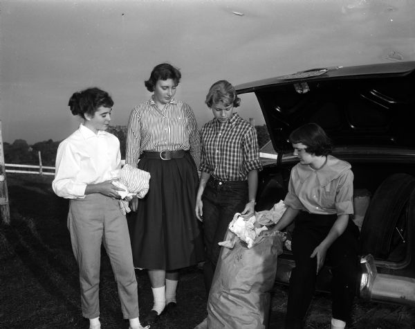 Outdoor group portrait of four members of the Madison Hunt Club with a rag collection to help pay for a trip to Chicago to attend the Grand International Horse Show. The high school girls in the picture are, left to right: Kathy Knechtjes of Edgewood, Val Taylor of Wisconsin High School, Sue Heebink of Wisconsin High School, and Elizabeth Jackson of Edgewood High School.