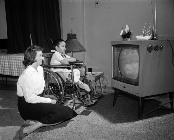 Student nurses in Madison take part in a state-wide aid project at various hospitals and welfare centers during Student Nurse Week. Susan Miller of Methodist Hospital joins Glen Gilley (seated in a wheelchair) to watch a television program at the Wisconsin Neurological Foundation.