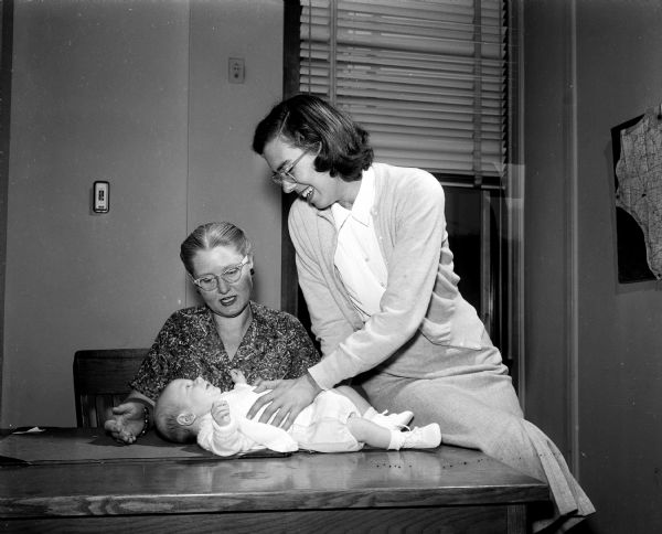 Mrs. Elizabeth Siska, district supervisor with Children's Service Society, and Miss Ann Clark, a case worker, are shown with a ten-week-old baby boy to be adopted. The society is one of the Red Feather services supported by the United Givers' Fund.