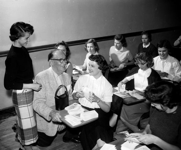 Slightly elevated view of Joseph R. (Roundy) Coughlin posing with members of the Madison West High School girls' club who stuffed envelopes for "Roundy's Fun Fund."