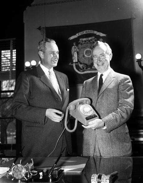 The original caption states: "the Wisconsin Telephone Co.'s one-millionth telephone now in service was presented to Gov. Vernon W. Thomson by Charles E. Wampler, president of the company. The green-colored telephone was installed in the governor's Wisconsin State Capitol office during a brief ceremony. It came complete with a narrow, gold band inscription and special plate bearing the state seal. The company observed another milestone earlier this year when it completed 75 years of service throughout the state."
