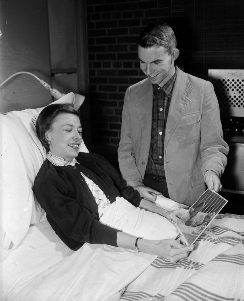 Portrait of Phyllis Kauffman, a tuberculosis patient at Lake View Sanatorium, with her husband, Robert, taken while he shows her pictures of their 7-month old baby. Mrs. Kauffman expects to be confined to Lake View from 16 months to two years.