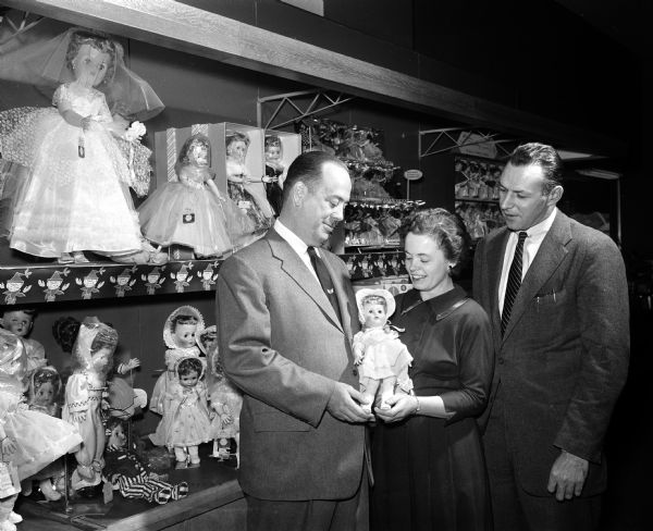 Empty Stocking Club's gift wrapping committee posing amidst dolls on display at Sear's toy department. Left to right: E.L. Diener, manager of the Sears store; Phyllis Wikoff, director of the Empty Stocking Club; and Maj. Robert Perina, commandant of the Marine Corps Reserves unit.