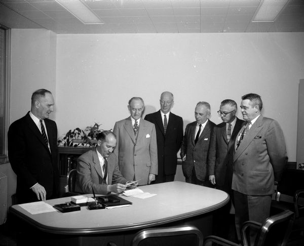 Mayor Ivan A. Nestingen, seated, receives a $325,000 check as payment for the purchase of the city's contagious hospital at 1954 East Washington Avenue by the Wisconsin Neurological Foundation. Standing, left to right: Harold E. Hanson, City Attorney; and representatives of the foundation, Dr. William A. Werrell, president; Randolph Conners, attorney; Dr. Edward P. Roemer, director; Donovan Eastin, executive director; and Attorney John P. Roemer, Milwaukee, vice-president.