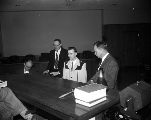 The original caption states, "Edward Krueger, center, is shown as he was sentenced by Circuit Judge Richard Bardwell to five years in Green Bay state reformatory for his part in the Lark Lanes burglary when Ralph O'Dell fatally shot a pinsetter there.  Beside Krueger are Asst. Dist. Atty. Richard Cates, left, and Atty. Vernon Molbreak, Krueger's counsel."  Krueger (center) is wearing a tie and a two-toned suit jacket with a dark yoke.