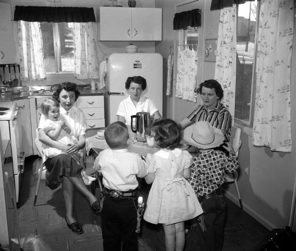 Monona Village homemakers share their weekday coffee hour at the home of Mrs. Randall Wind. Mrs. Wind holds her daughter Lori, age 2. Guests are Mrs. John O. Dahl and Elizabeth Smith. Children in foreground, left to right, include John Dahl, Jr. 4; Randi Jo Wind, 4; and Danny Lee Smith, 3.