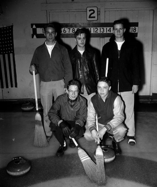 Five teen boys from the West High School Fred Nelson Curling Rink team posing with brooms. Shown in the front row are Don Lautz and Rick Wheeler. In the back row are John Weinlick. Nelson, and Craig Washa. They won the Madison High School curling tournament when they defeated the Wisconsin High School Dave Strobel Rink Team, 7-5.