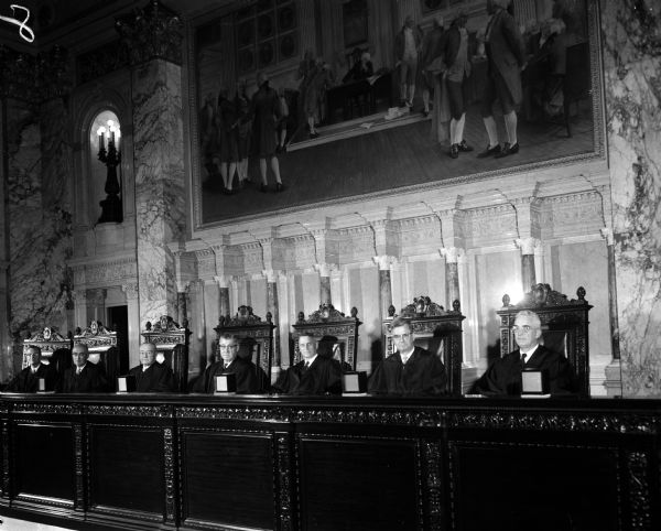 Portrait of the seven Wisconsin Supreme Court judges sitting in the Supreme Court Chamber at the Wisconsin State Capitol Building. The justices, seated left to right, are Thomas E. Fairchild, George R. Currie, Grover L. Broadfoot, Chief Justice John E. Martin, Timothy E. Brown, Emmert L. Wingert, and E. Harold Hallows.