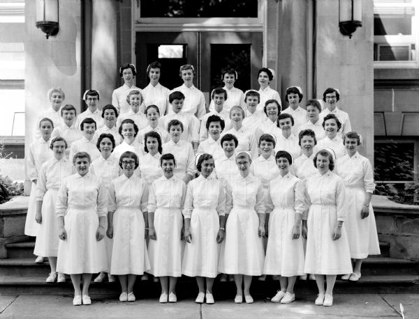 Group portrait of the 1958 graduating class of nurses from St. Mary's Hospital School of Nursing. They are wearing white uniforms and caps with a black stripe.