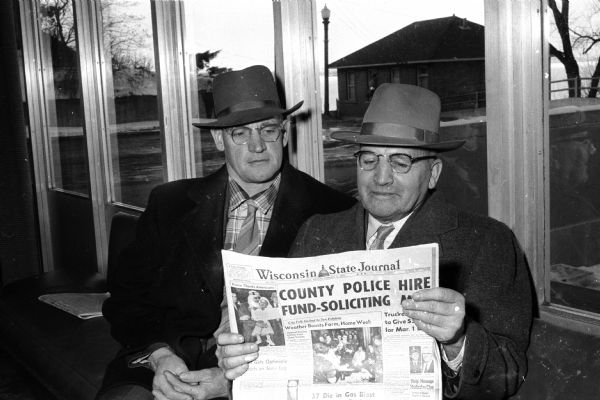 Walter Ladwig of Juda (left) and Oscar Wold of Hillsboro reading The "Wisconsin State Journal" between sessions at the annual University of Wisconsin's Farm and Home Week. The men are sitting in front of windows with a view towards Lake Mendota.