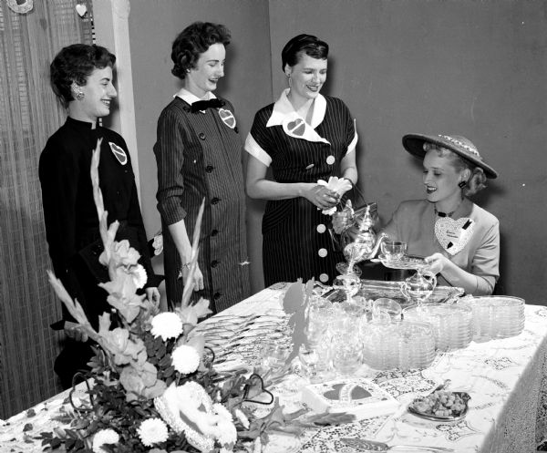 Four women gather around the table during a St. Valentine's Day tea given by the Truaz Officer's Wives Club to welcome wives of officers newly assigned to Truax Field Air Force Base. Mrs. Frederick Nelander, wife of the base commander, is pouring tea for, left to right Caroline Dahl, Clare Roberts, and Mrs. Earl Doeren.