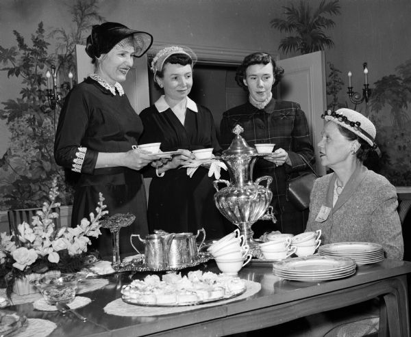 First vice-president of the Wisconsin League of Women Voters, Mrs. Ernest T. Clough of Milwaukee, serving tea at the executive mansion after a session at the Wisconsin State Capitol for the league's legislative school. Standing, left to right, are: Mrs. Bonnie Kienitz, Mrs. Martha Schmidt, and Mrs. Evelyn Werner, all of Madison.