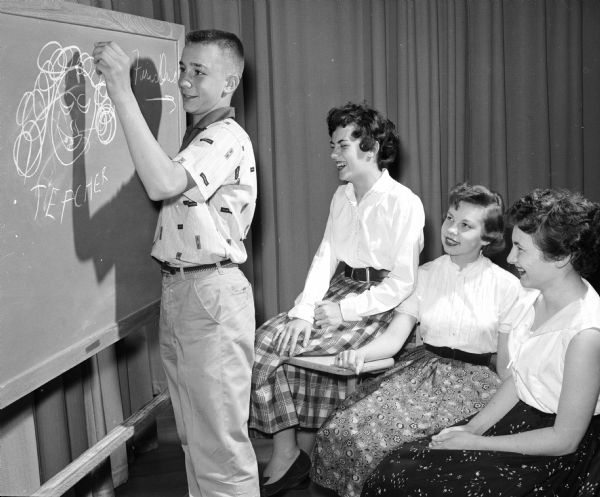 James Shipley pretends to draw while his fellow pretend pupils, (left to right): Doris Breunig, Ruth Dahik, and Jackie Reisdorf, look on at the Middleton High School fashion show.